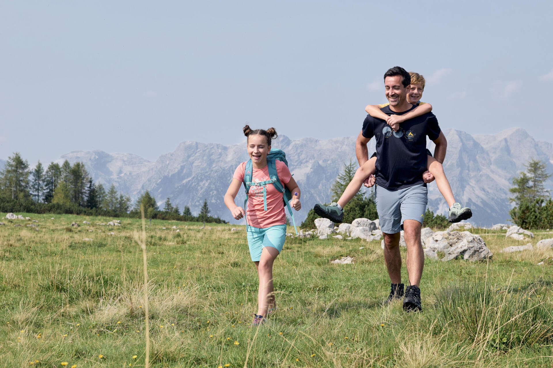 Ein Vater beim Wandern mit seinen zwei Kindern. Den Sohn trägt er am Rücken.