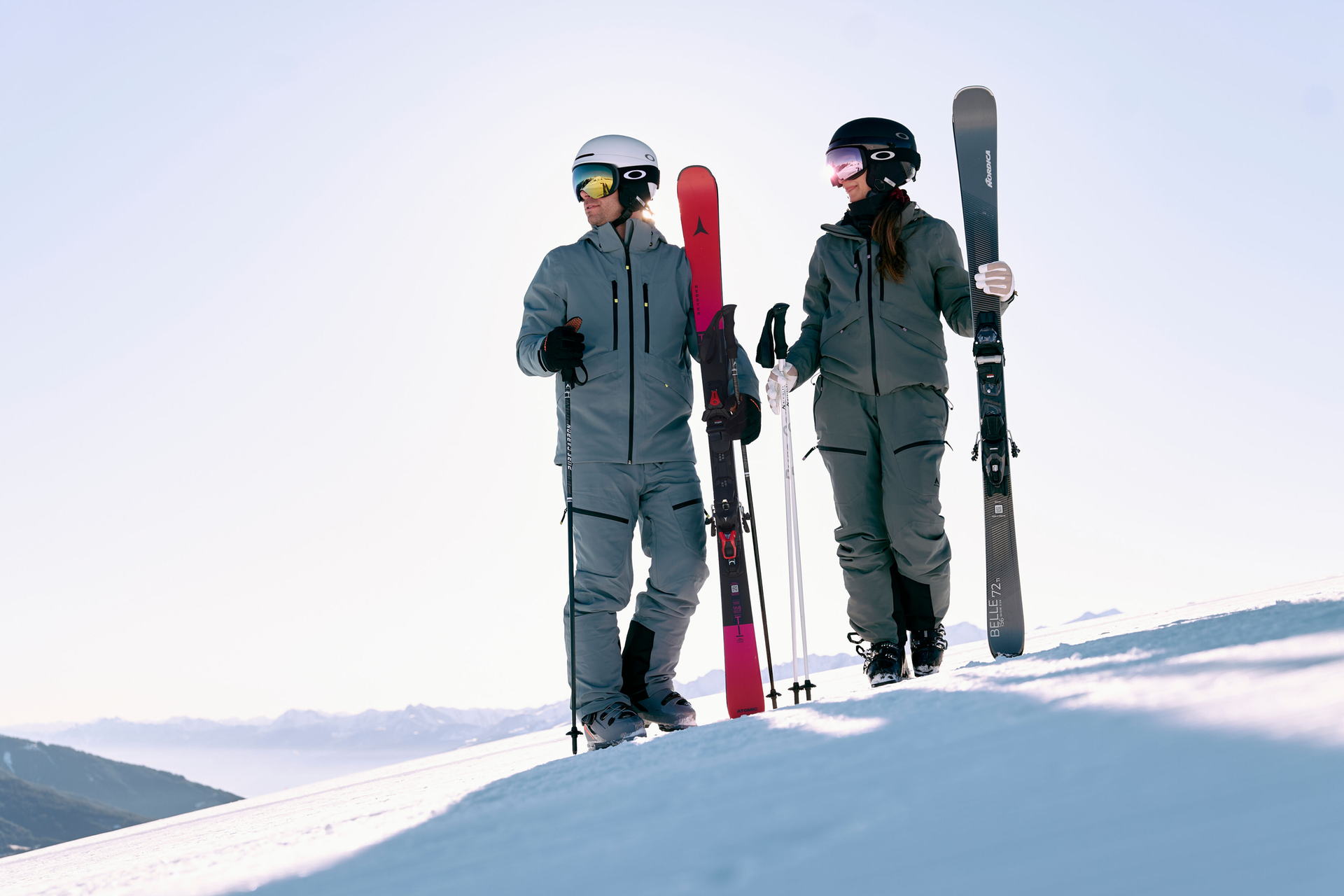 Vier Skifahrer strecken sich bei Sonnenaufgang auf einem verschneiten Berghang, umrahmt von majestätischen, schneebedeckten Gipfeln unter einem klaren Himmel, und vermitteln ein Gefühl von Gelassenheit und Abenteuer.