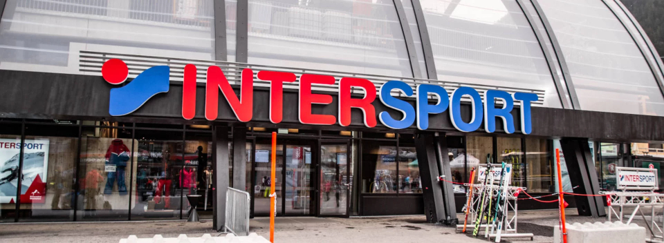 Storefront of Intersport with large red and blue signage. Glass facade displays sports equipment. Snow on the ground adds a wintery feel.