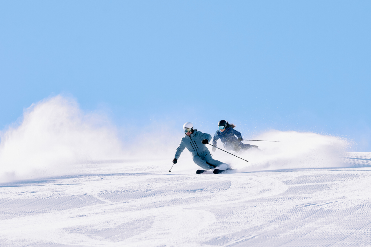 Schneebedeckte Berge unter einem klaren Himmel, mit Bäumen und einer kleinen Hütte im Vordergrund. Die ruhige, unberührte Landschaft strahlt Gelassenheit aus.