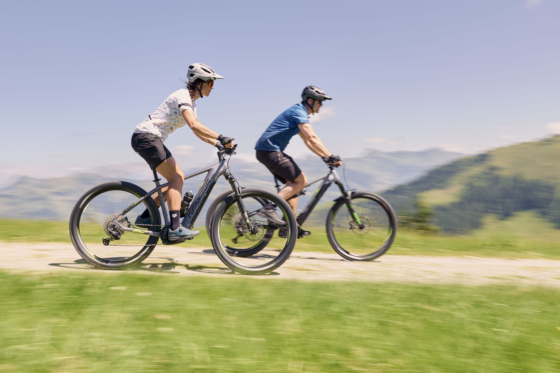 Ein Radfahrer steht auf einer felsigen Klippe und hebt sich vor dem klaren blauen Himmel mit einem leuchtenden Sonnenuntergang ab. Die Szene vermittelt ein Gefühl von Abenteuer und Ruhe.