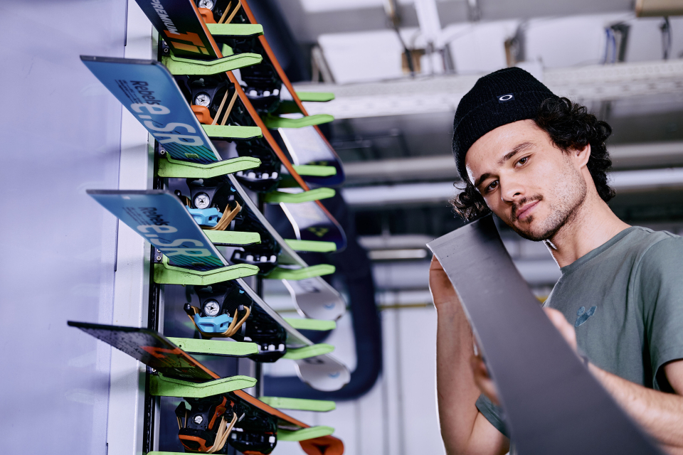 Ein geräumiger Skiraum mit weißen Schließfächern und Bänken. Eine Person sitzt da und passt ihre Skischuhe an. Die Skier lehnen an einem Schließfach und vermitteln eine ruhige, aufgeräumte Atmosphäre.