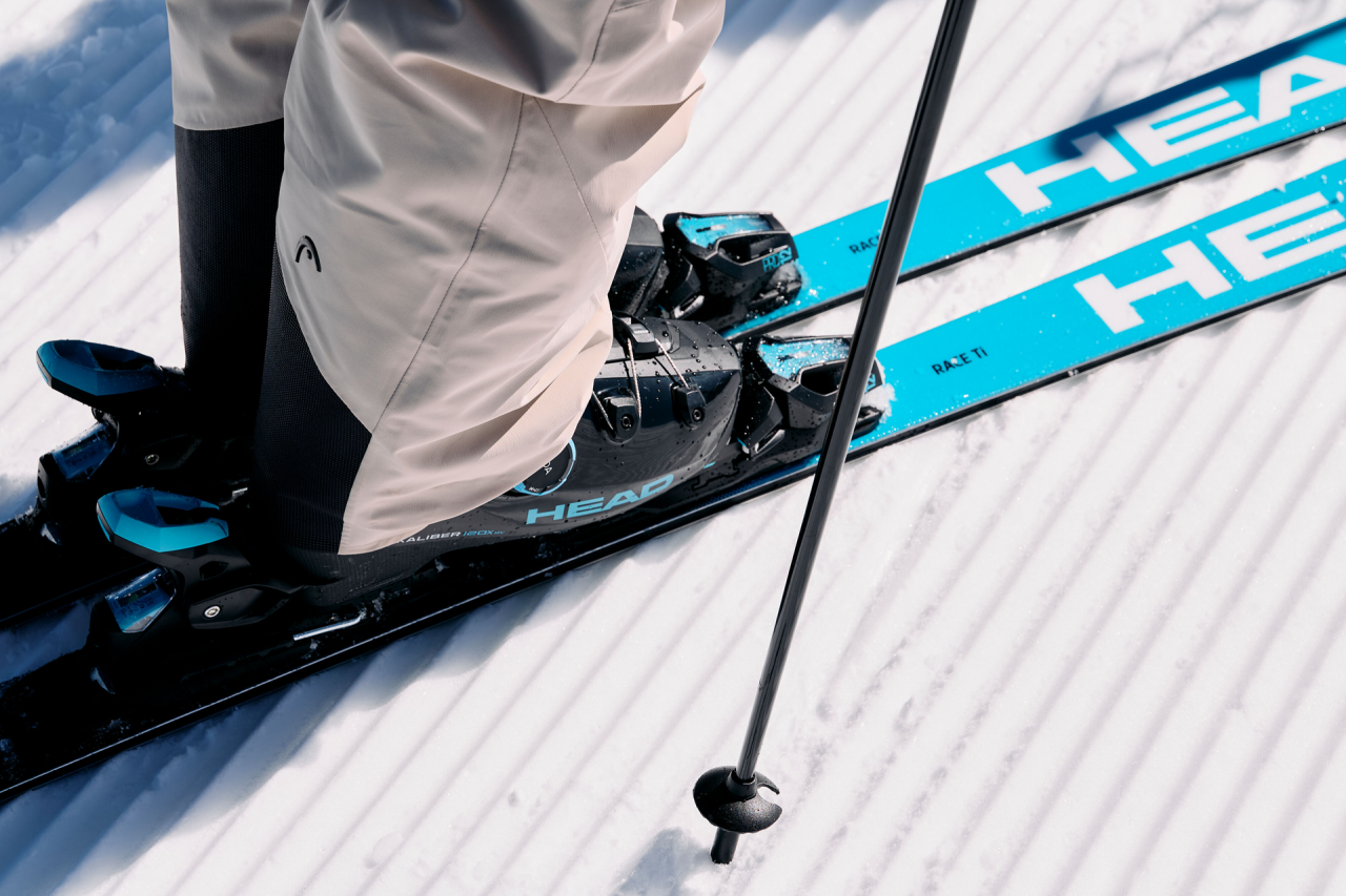 Two skiers in colorful gear race down a snowy slope against a backdrop of sunlit mountains, conveying energy and excitement.