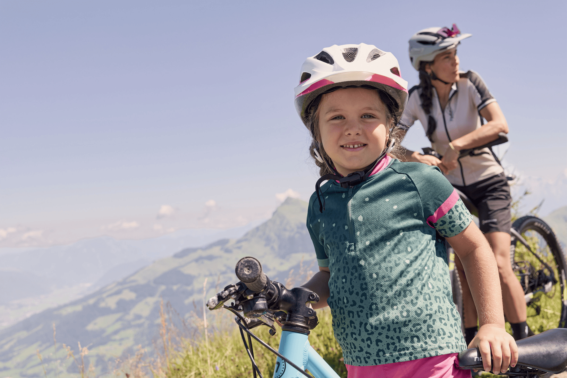 Ein Kind und ein Erwachsener, beide mit Helmen, besteigen einen felsigen Berg unter einem teilweise bewölkten Himmel. Das Kind befindet sich im Vordergrund, konzentriert und mit der Sicherheitsausrüstung fest umklammert.