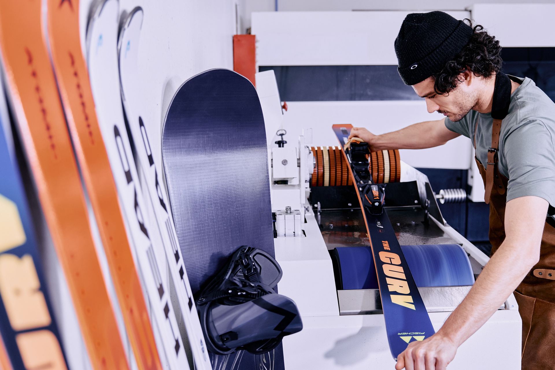 Person sharpening a snowboard edge with a grinding tool, producing sparks. The snowboard is yellow. The scene conveys focus and precision.
