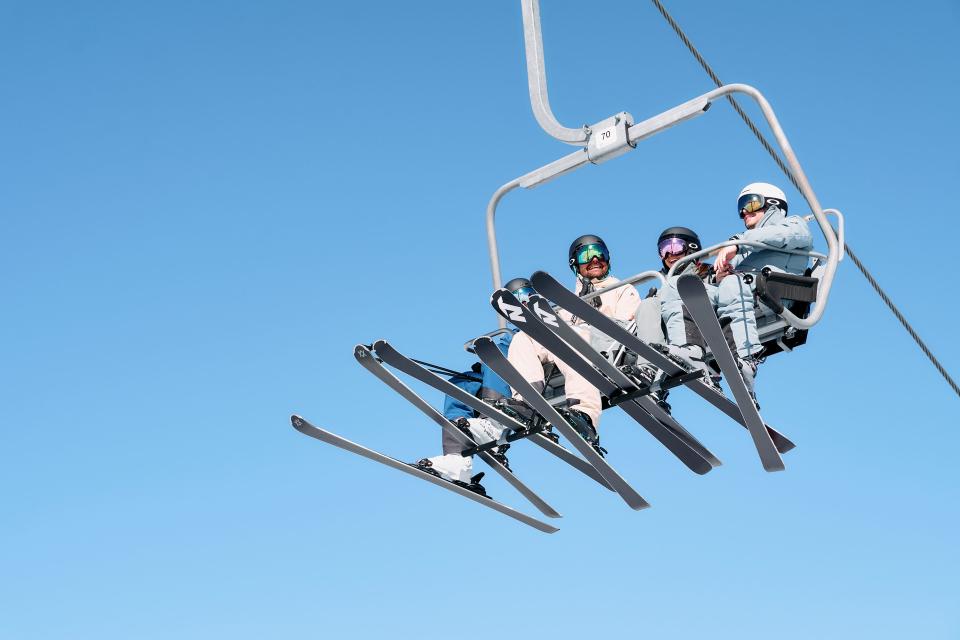Eine rote Seilbahn fährt unter einem klaren Himmel über schneebedeckte Berge und einen blauen See und vermittelt ein Gefühl von Entdeckungslust und Ruhe in einer Winterlandschaft.