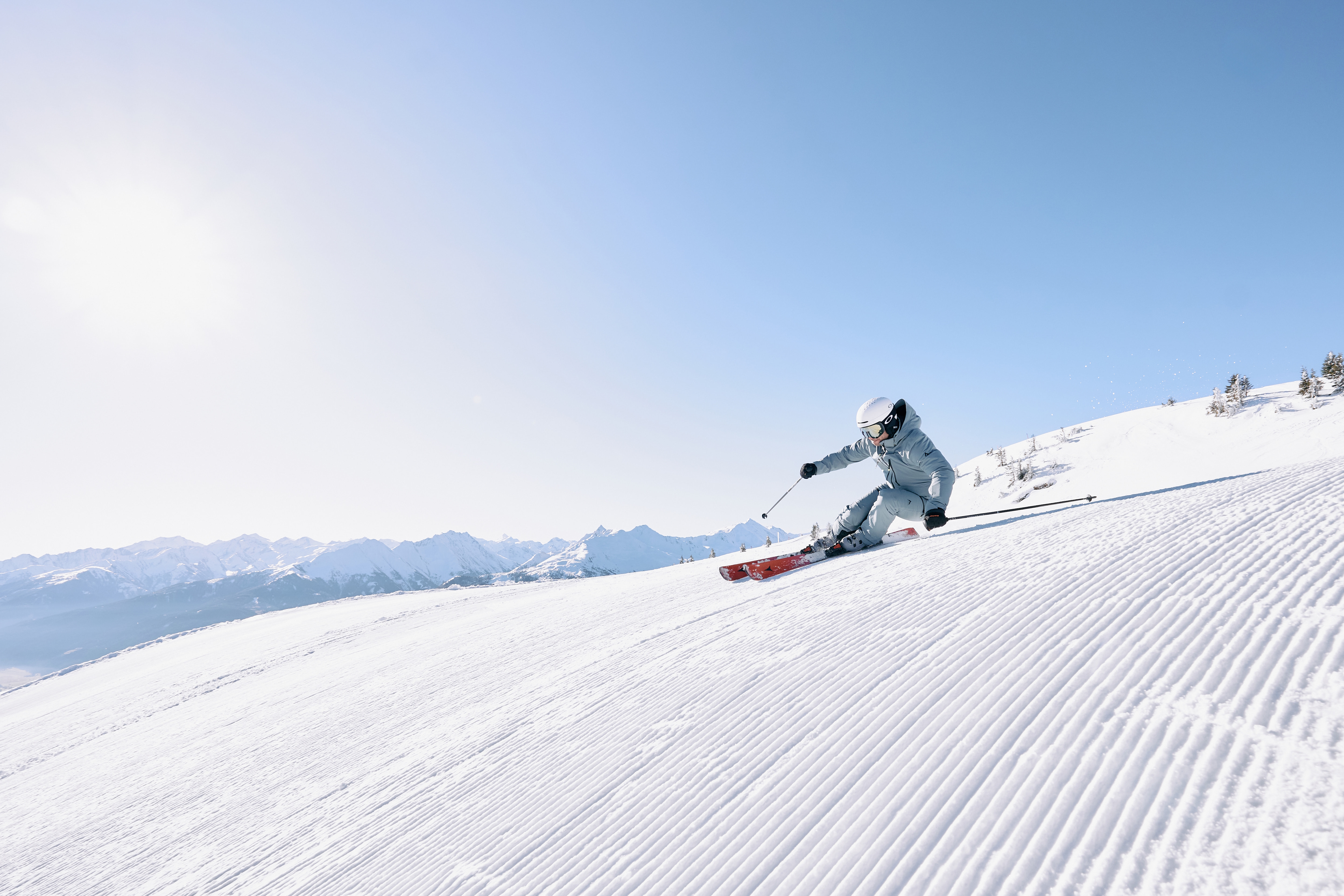 Woman skiing on a groomed slope under a bright sun in a wintery mountain landscape.