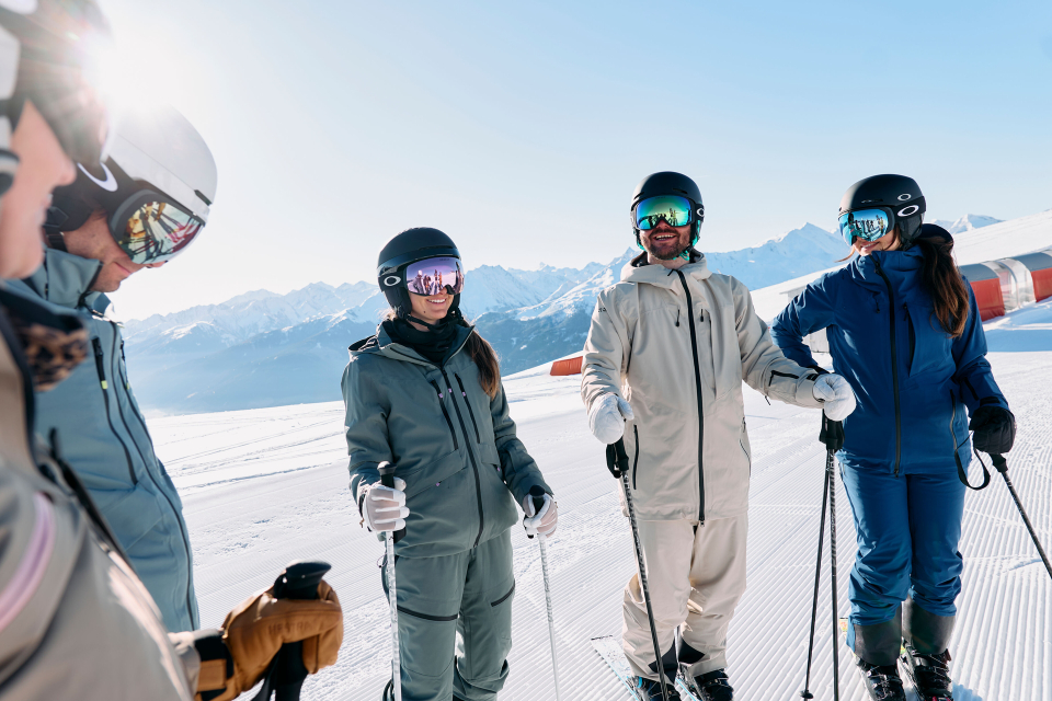 Text „RENT“ mit einem Skifahrer in Blau und Gelb, der zwischen den Buchstaben Ski fährt. „INTERSPORT“ in kleiner Schrift darüber. Der Hintergrund zeigt schneebedeckte Berge und Bäume.