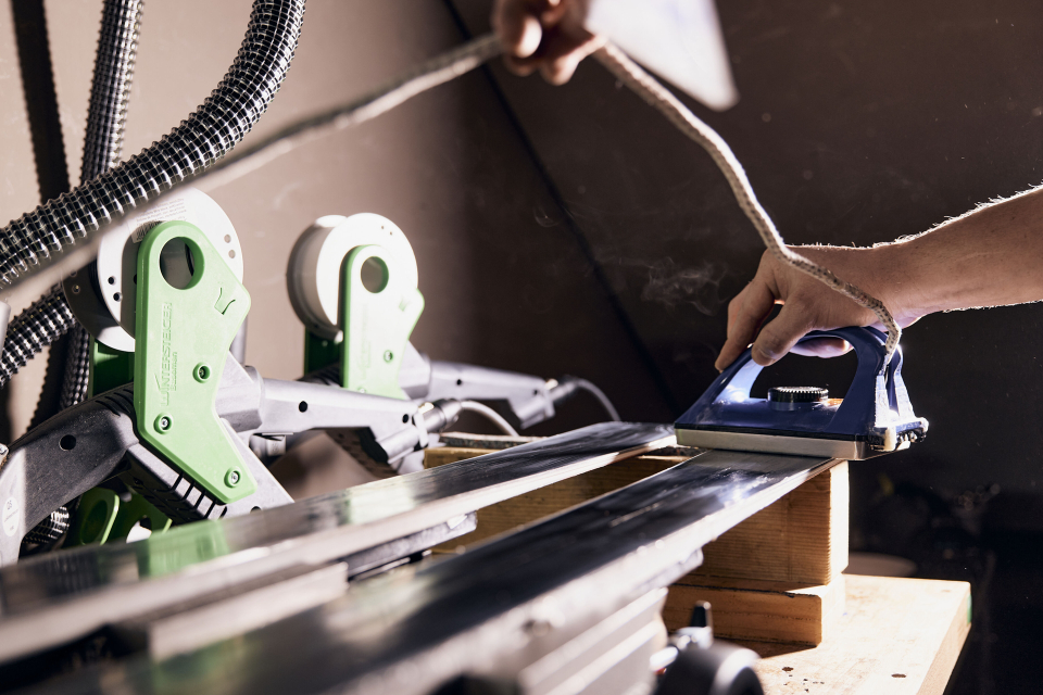Close-up of an industrial machine in operation, featuring metallic parts, blue cables, and water spraying, creating a dynamic and technical atmosphere.